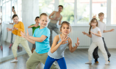 Dynamic little boy and girl training Rock-and-Roll dance poses in pair together with other...
