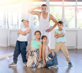 Cheerful preteen children, boys and girls, striking dynamic dance poses with young male instructor...