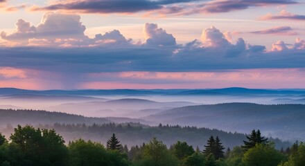 Fototapeta premium Panoramic view of a misty forest and rolling hills under a dramatic sunset sky with pink and blue hues. The scene evokes tranquility and vastness.