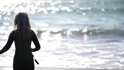 Woman in wetsuit looking at the ocean on a sunny day.