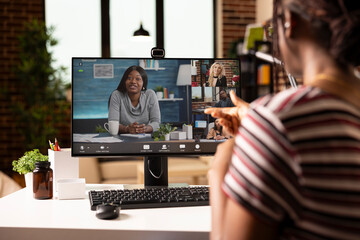 Back view of businesswoman in home workspace, discussing project plans with teammates in video...