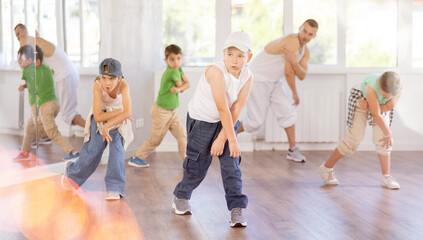 Fototapeta premium Preteen boy performing hip hop dance moves, showcasing skills and concentration, during group class for kids led by young male instructor in street dance studio