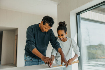 Grandfather teaching granddaughter to measure wooden plank while renovating house