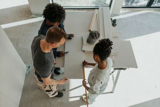 High angle view of children helping father while measuring wooden plank on table