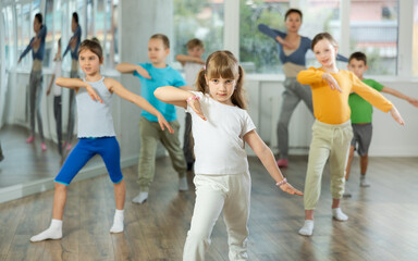 Girl learns to dance during childrens master class in studio. Teacher watches students, participates in training in background