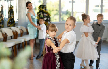 Joyful minor schoolboys and schoolgirls training valse dance in events salon adorned with Xmas tree