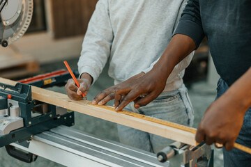 Midsection of senior man using tape measure while granddaughter marking with pencil on wooden plank