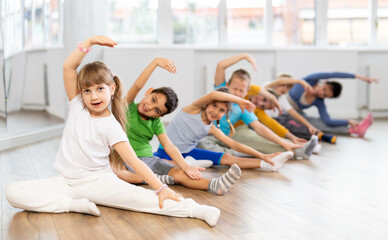 Little school age children learn to do dance moves on the floor in a choreography studio