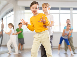 Positive juvenile boy and girl engaged in Rock-n-Roll dance in pair together with other children...