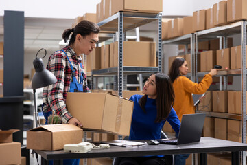 Asian workers team handles business logistics in a compact inventory room, taping boxes and...