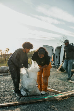 Mother and son collecting construction waste in trash bags outside house at sunny day