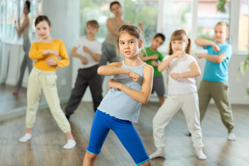 Positive juvenile girl engaged in breakdancing together with children's group in training room...