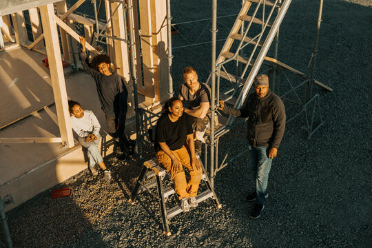 High angle view of multiracial family members sitting outside incomplete house at sunny day