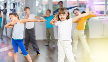 Dynamic little girl training hip hop dance poses with instructor and other attendees of dancing...