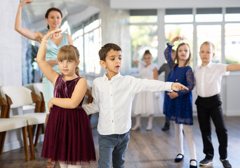 Enthusiastic preteen children, boys and girls in party attire performing elegant waltz in pairs in...
