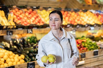 Portrait of female shopper carefully selecting ripe apples on a supermarket display