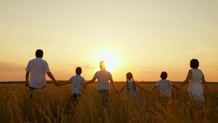 Parents children go holding hands walk through wheat field. Happy family of farmers walk in nature, sunset. Teamwork group of people travel walk wheat field. Group of people in nature sunny day, kids