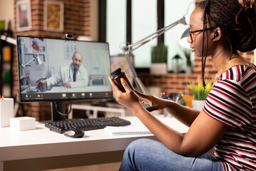 African american woman sitting at home desk having online medical consultation on desktop pc. Black...