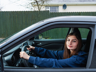 A young inexperienced woman is driving a car with her sunglasses on. She is wearing a blue hoodie....