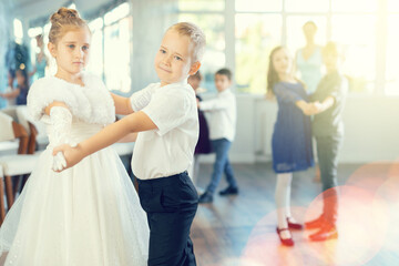 Joyful schoolboys and schoolgirls of primary classes training valse dance in events salon