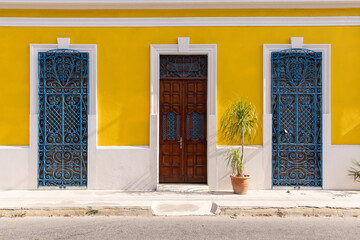 Traditional Yucatan architectural elements in Mexico - bright yellow wall, blue doors, and potted plants.