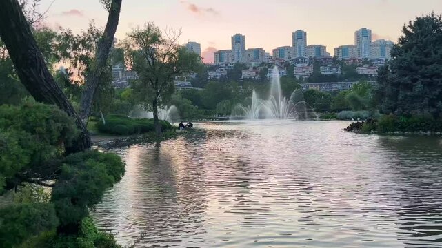 Two people resting silhouette with lake park view and behind modern buildings silhouette at sunset in Istanbul, Turkey. (4K video)
