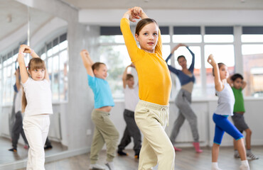 Active preteen girl practicing sport dances with other children and teacher during dancing classes