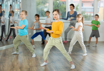 Fototapeta premium Girls with boys repeat teaches sequences of movements during training, train to perform electro dance, enjoys active hobby to favorite music. Unrecognizable female teacher administer conduct class