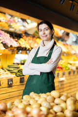 Young woman seller in apron offers potatoes in vegetable shop