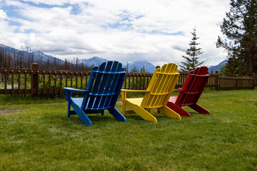 Muskoka chairs lined up along grass, blue yellow red
