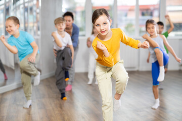 Children studying modern style dances with female teacher in dance class indoors