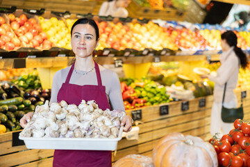 Saleswoman holds a plastic container with garlic in her hands and prepares to lay it out on the counter in the supermarket