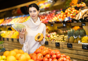Young woman buyer choosing fresh papaya in vegetable shop