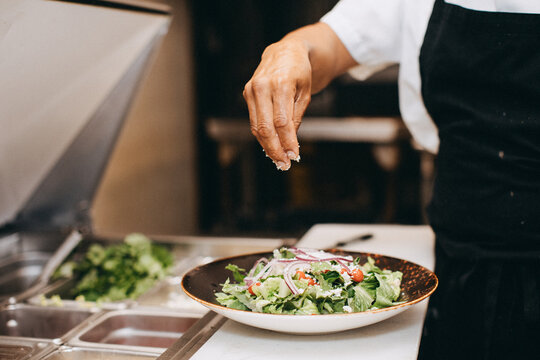 A Cook Sprinkles Cheese on a Salad in a Restaurant Kitchen