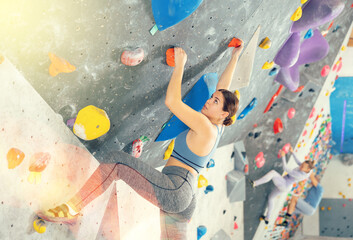 Focused sporty young girl climbing on bouldering wall demonstrating physical strength, technical...