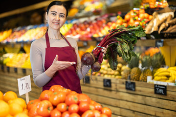 Female grocery store worker offers ripe beet in grocery department of the supermarket