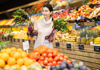 Young woman buyer choosing fresh beets in vegetable shop