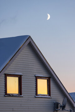Snow-covered house roof with glowing windows and crescent moon