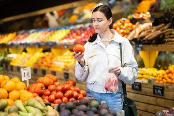 Woman carefully selects fresh tomatoes, standing near the counter in the supermarket