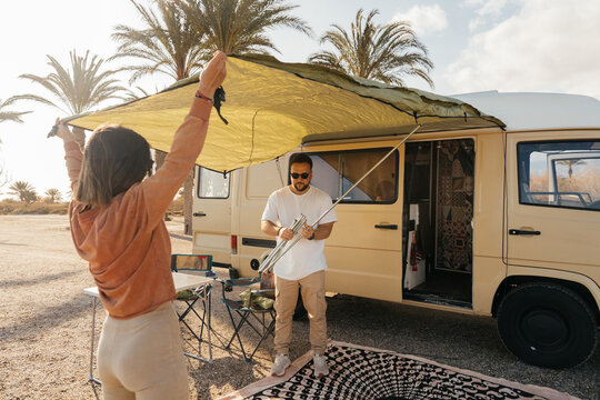 Couple setting up awning on camper van in palm tree setting
