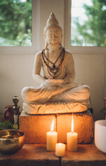 Detail of Buddhist altar with candles, plants and a huge Buddha in the center.
