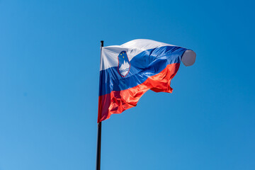 Slovenian flag waving in the wind against blue sky