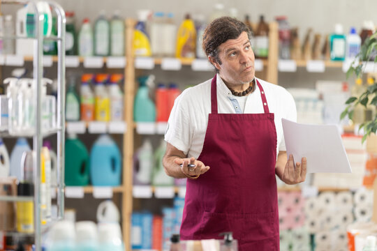 Disappointed salesman reads paper documents, analyzes unsatisfactory work results. Man upset by sales data, comes up with solution