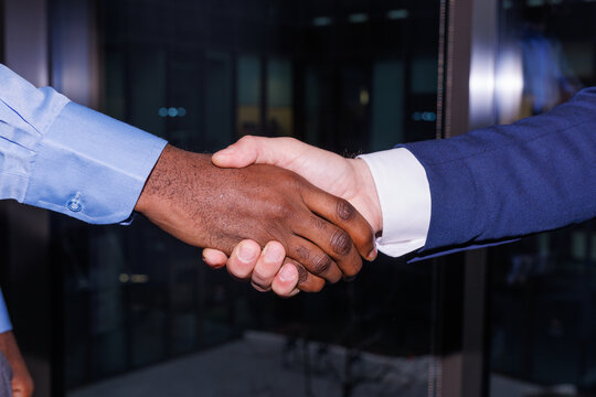 Anonymous business partners shaking hands in office near window