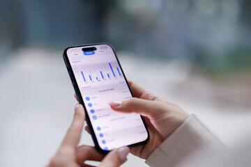 Anonymous woman tapping screen of smartphone and examining charts