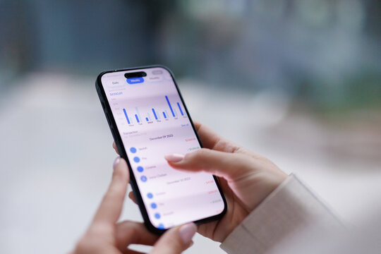 Anonymous woman tapping screen of smartphone and examining charts