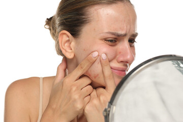Studio shot of young woman with acne squeezing pimples in pain, isolated on white background