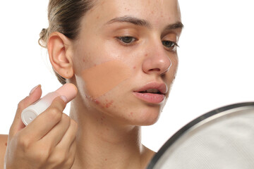Young woman applying concealer on acne-prone skin, studio shot on white background