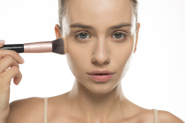 Young woman applying foundation with makeup brush, studio shot on white background
