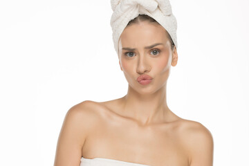 Funny young woman with towel on head making silly face after spa treatment, studio shot on white background